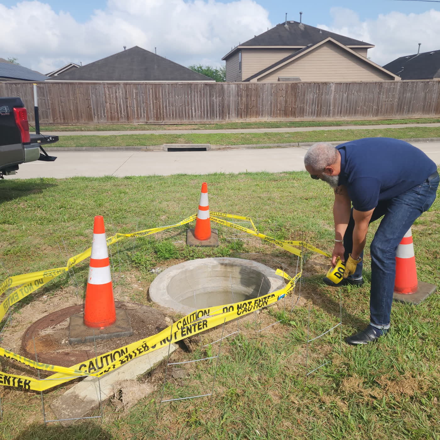 Tahir Charles taping off an open manhole in a residential street, marked with cones and caution tape